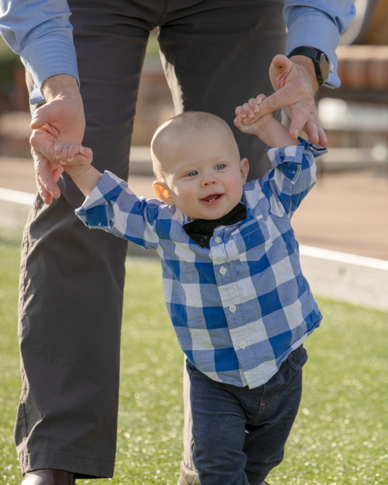 baby with bowtie walking holding dad's hands